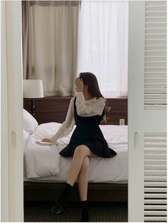 a woman sitting on top of a bed next to a white window sill in a bedroom