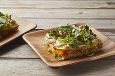 two plates with sandwiches on them sitting on a wooden table, one has lettuce and tomato