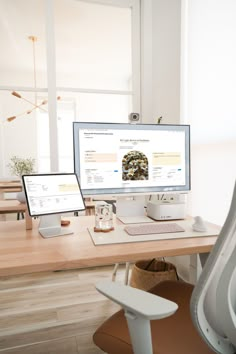 two computer monitors sitting on top of a wooden desk in front of a white chair