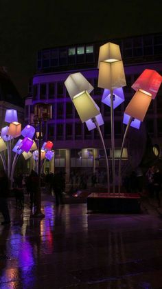 people are walking around in the rain at night with colorful lights on them and umbrellas