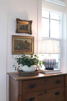 a table with a lamp, potted plant and pictures on the wall above it