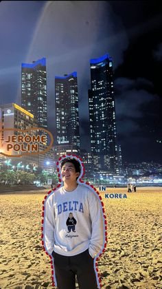 a young man standing on top of a sandy beach next to tall buildings at night