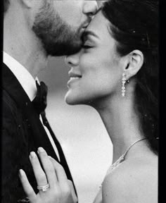 black and white photograph of a bride and groom kissing each other with their wedding rings on their fingers