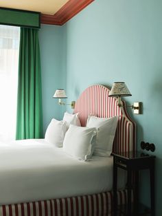 a bed with white and red sheets in a bedroom next to a window covered by green curtains