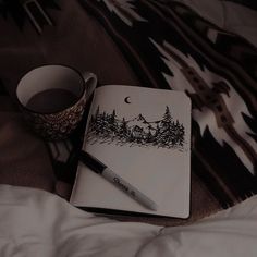 a notebook, pen and cup sitting on top of a bed next to each other