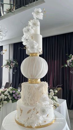 a three tiered white and gold wedding cake on top of a table with flowers