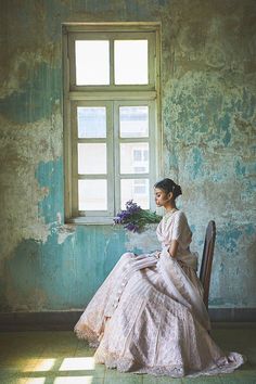 a woman sitting on a chair in front of a window holding a bouquet of flowers