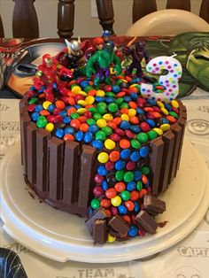 a birthday cake with chocolate frosting and colorful candies on the top, sitting on a plate