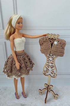 a doll is holding up a crocheted dress