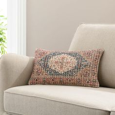 a couch with a pillow on top of it in front of a window and potted plant