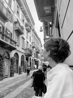 black and white photograph of people walking down an alleyway with buildings in the background