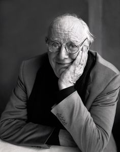 black and white photo of an older man with glasses sitting at a table in front of a window