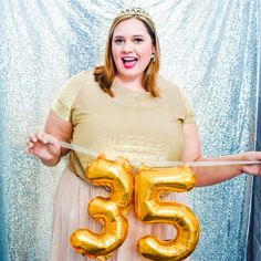 a woman in a dress is holding two gold balloons that say 35 and the number fifty five