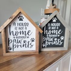 two small wooden houses sitting on top of a counter next to each other, one has a dog's paw print and the other has a house is not a home