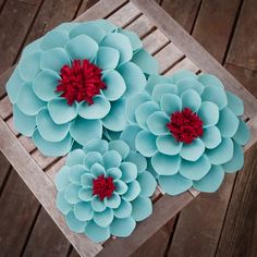 three large blue flowers with red centers on a wooden table next to wood planks