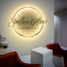 the salon logo is illuminated on the wall above two red chairs and a white sink