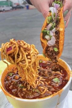 a person is holding a spoon full of noodles and meat in a large white bowl