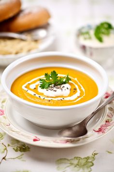 a white bowl filled with carrot soup on top of a floral table cloth next to other plates