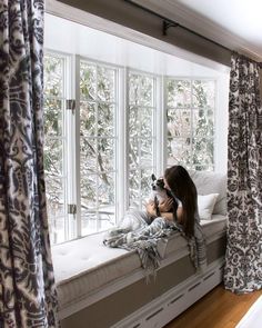 a woman sitting on top of a window sill holding a stuffed animal in her lap