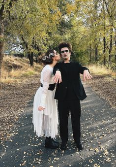 a man and woman dressed up in costumes standing on a road with trees behind them