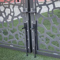 an iron gate with decorative designs on the top and bottom, in front of a grassy area