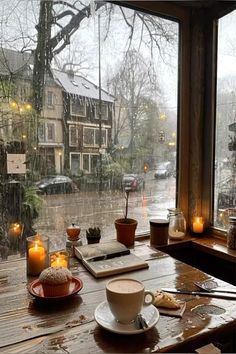 a cup of coffee sitting on top of a wooden table next to a window covered in rain