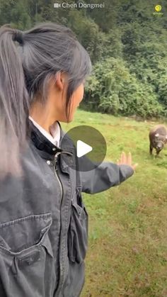 a woman standing on top of a lush green field next to an animal in the distance