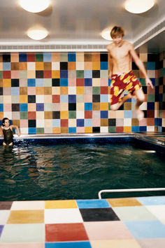 two people in a swimming pool with multicolored tiles on the wall