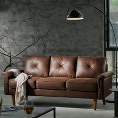 a brown leather couch sitting in a living room next to a table with a vase on it