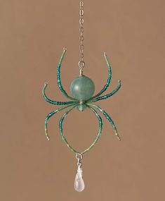 a green beaded spider hanging from a chain with a pearl drop on it's end