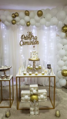 a table that has some cake on it and white balloons hanging from the ceiling behind it