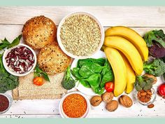 an assortment of food including bread, fruits and vegetables on a white wooden table top