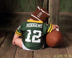 a baby sitting on the floor with a football in his hands and wearing a green jersey