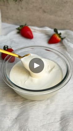 a glass bowl filled with yogurt next to strawberries on a white cloth