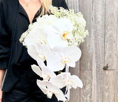 a woman holding a bouquet of white flowers in front of a wooden wall with planks