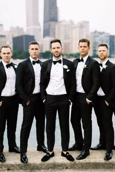 a group of men in tuxedos standing next to each other near the water