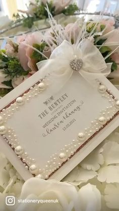 a wedding card with pearls and flowers on it sitting on a bed of white roses