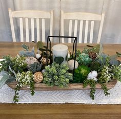 an arrangement of greenery and candles sits on a table in front of two chairs