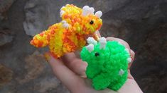 two small toy animals sitting on top of each other in their hands, one is green and the other is orange