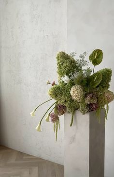 a vase with flowers and greenery in it sitting on a wooden floor next to a wall