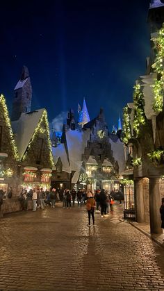 people are walking around in front of the wizard's castle at night with christmas lights