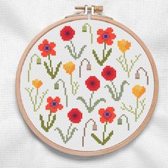 a cross stitch pattern with red, yellow and orange flowers on white fabric behind a wooden hoop