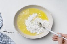 someone is mixing ingredients in a bowl with a spoon on the table next to it