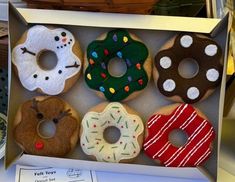 six decorated doughnuts in a box on a table