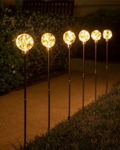 five solar powered garden lights on the ground in front of some grass and bushes at night