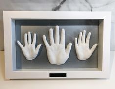 three white hands in a shadow box on a marble countertop, with one holding the other's hand