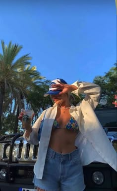 a woman standing in front of a car with her hands on her head and holding a drink