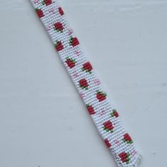 a white beaded bracelet with red roses and green leaves on the end is shown