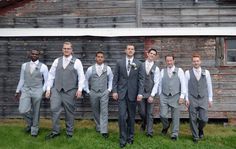 a group of men standing next to each other in front of a wooden building and grass