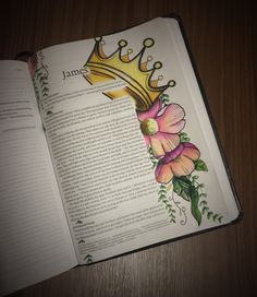 an open book with flowers and a crown painted on the pages, sitting on a wooden table